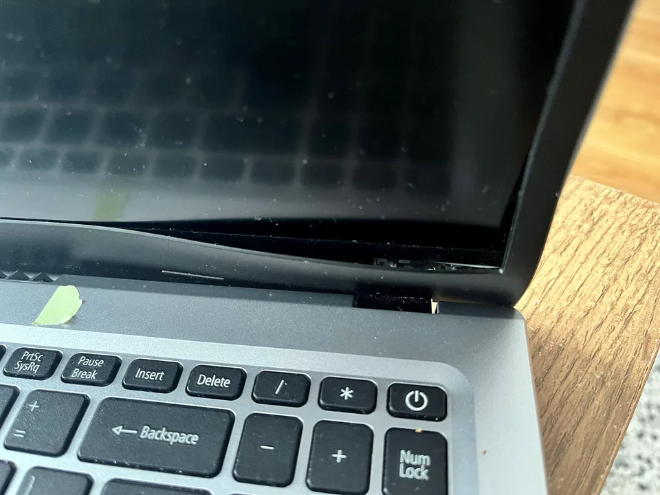 Broken laptop hinge and screen casing being inspected before repair
